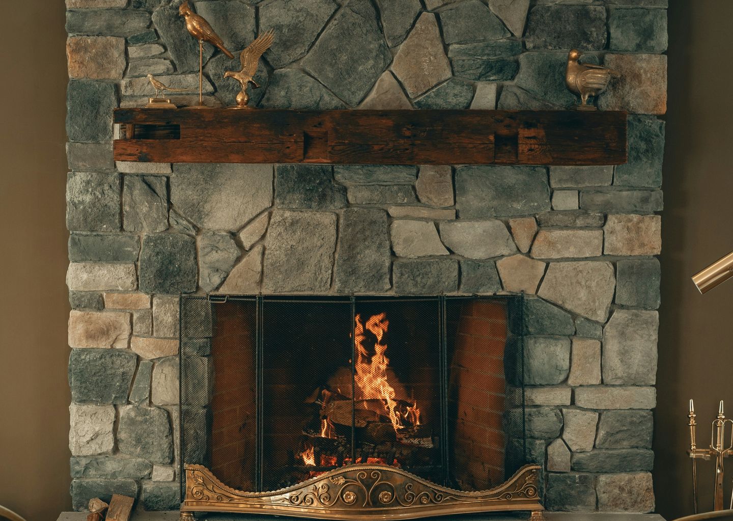 A fire crackling in a stone fireplace beneath a rough timber mantel lined with brass birds.